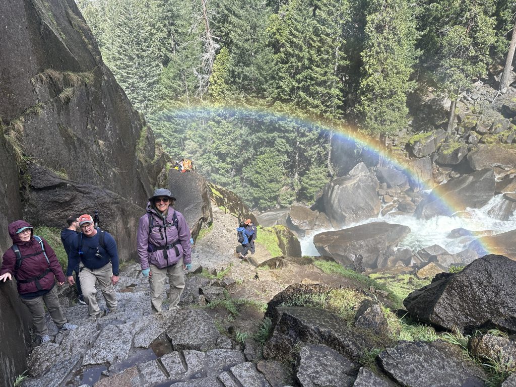 Hiking up the wet granite steps of the Mist Trail below Vernal Falls in Yosemite with a rainbow in the background