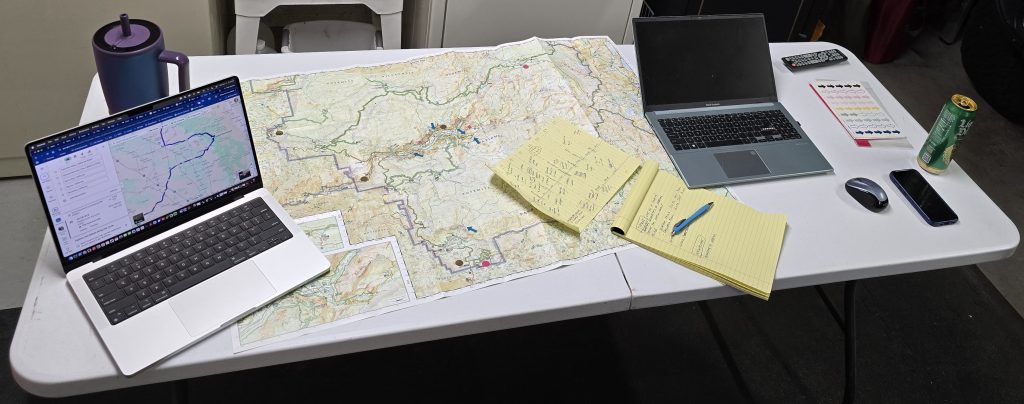Trip-planning with paper map, laptops, notepad, and pen spread out on the table